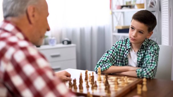 Young boy playing chess with grandfather, family traditions, mind development - 写真・画像