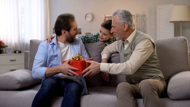 Grandfather and schoolboy congratulating middle-aged man and giving red gift box - Zdjęcie, obraz