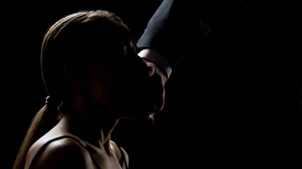 Man closing mouth to humiliated girl against black background, kidnapping victim - Valokuva, kuva