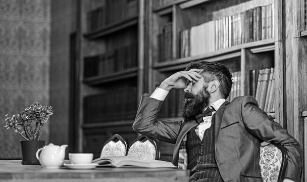 Man has terrible headache. Bearded man in formal suit suffers from negative thoughts and looks unsatisfaied. Mature man with tired face has afternoon tea. Headache, bad mood, pain, emotions concept - Photo, Image