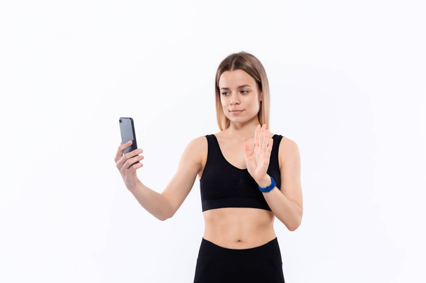 Młoda sportowa blond kobieta w czarnej odzieży sportowej co selfie z smartphone po treningu stoi na białym tle. - Zdjęcie, obraz