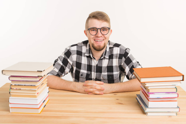 People, knowledge and education concept - smiling man sitting at the wooden table with books - 写真・画像