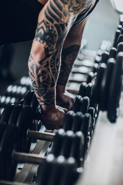 close up. male bodybuilder lifting dumbbells in gym - Zdjęcie, obraz