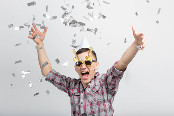 Люди, праздники и концепция вечеринки - веселый парень в очках танцует в конфетти на белом фоне
 - Фото, изображение