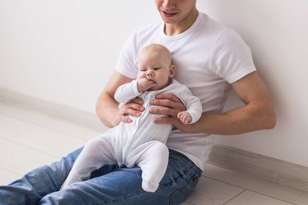 Βρέφος, την οικογένεια και την πατρότητα έννοια - ευτυχής πατέρας φαλακρός, κρατώντας το μωρό κόρη στο γόνατα σε λευκό φόντο - Φωτογραφία, εικόνα