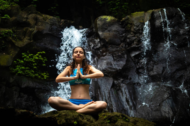 junge kaukasische Frau meditiert, praktiziert Yoga am Wasserfall in Ubud, Bali, Indonesien. Nahaufnahme. - Foto, Bild