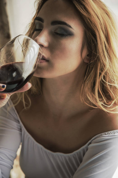 Νεαρή όμορφη γυναίκα με γυαλί κόκκινου κρασιού σε φως φόντο - Φωτογραφία, εικόνα