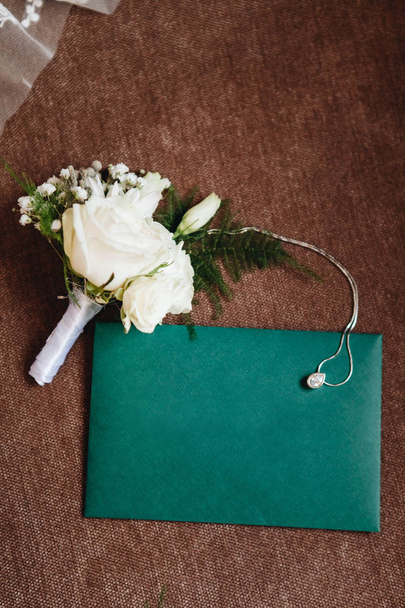 花嫁の結婚式の花束と銀のチェーンと暗い背景に緑の招待封筒 - 写真・画像