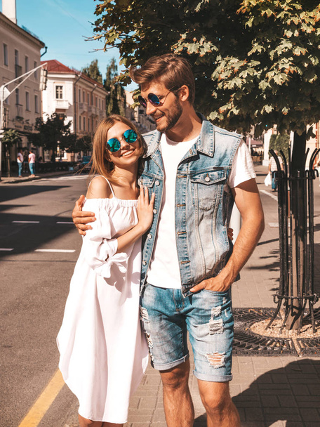 Smiling beautiful girl and her handsome boyfriend walking in the street. Woman in casual summer dress and man in jeans clothes. Happy cheerful couple family having fun in sunglasses - Photo, Image