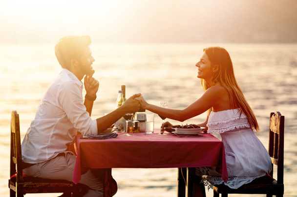 People, celebration, vacation, honeymoon and romance concept. Young couple enjoying a romantic evening dinner on the beach. - Foto, afbeelding