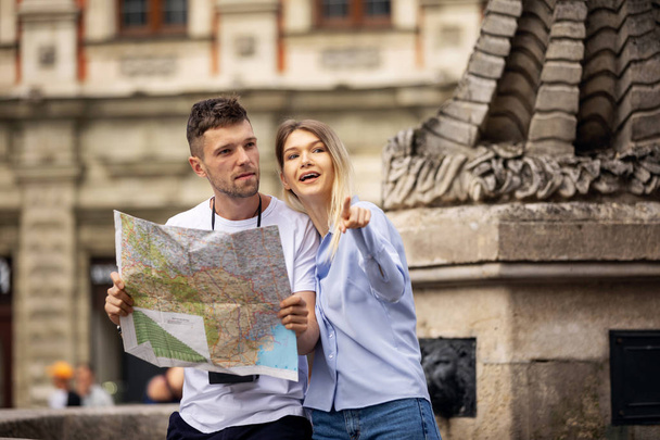 Couple With Map On Travel Vacations, Sightseeing. Happy Tourist Man And Woman In Stylish Clothes Traveling On Weekend, Walking With Map Around Streets. Tourism Concept. High Quality Image. - Valokuva, kuva