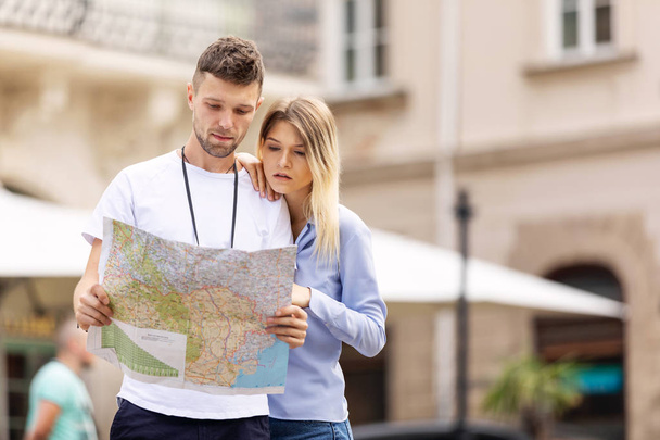 Couple With Map On Travel Vacations, Sightseeing. Happy Tourist Man And Woman In Stylish Clothes Traveling On Weekend, Walking With Map Around Streets. Tourism Concept. High Quality Image. - Foto, Bild