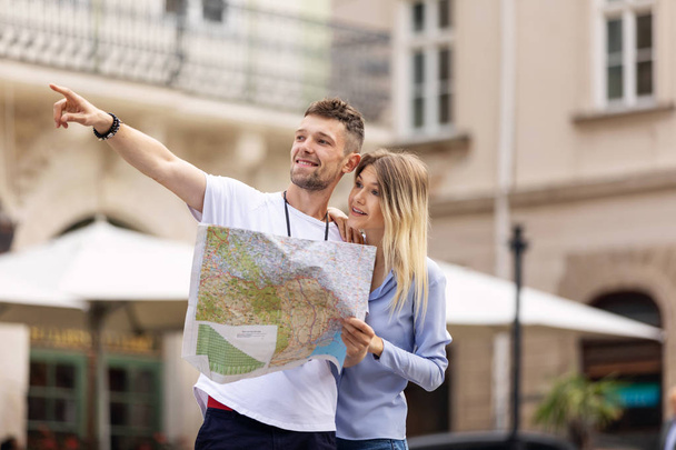 Couple With Map On Travel Vacations, Sightseeing. Happy Tourist Man And Woman In Stylish Clothes Traveling On Weekend, Walking With Map Around Streets. Tourism Concept. High Quality Image. - Photo, Image