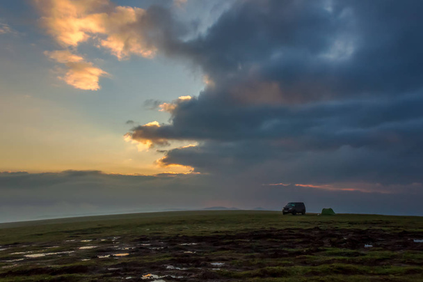 Landschap met het silhouet van een SUV en een tent bij zonsopgang, in een foto met weinig licht. Reizen met de auto is een idee voor uw avontuur in het wild, een wetenschappelijke expeditie of extreme reizen per SUV. - Foto, afbeelding