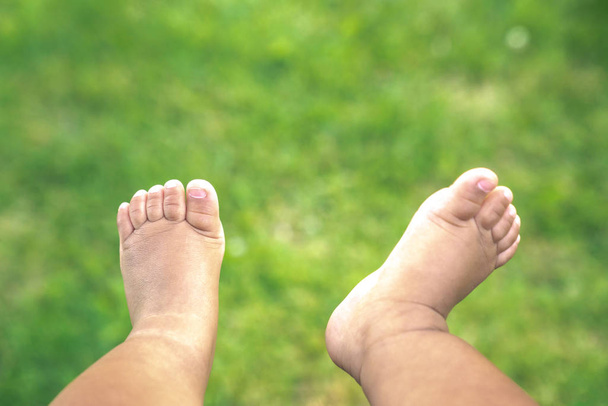 A close up of cute or adorable, bare skin chubby legs, feet and toes of a mixed race baby boy infant hanging down over lush green grass at a park on a sunny summer day. - Photo, Image