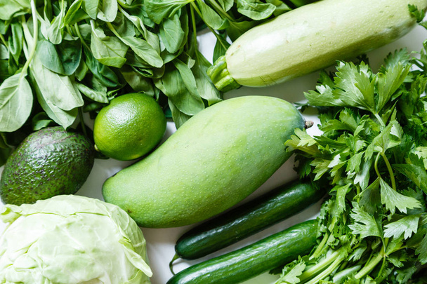 Fresh green vegetables variety on rustic white background from overhead, celery, avocado, cabbage, mango, cucumber, spinach, lime, squash. Healthy, vegetarian concept. Flat lay, top view - 写真・画像
