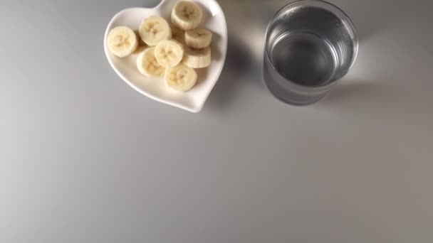 Sliced and whole bananas. On a white plate. On a gray background. Misted with clean water. The concept of a healthy lifestyle - Felvétel, videó