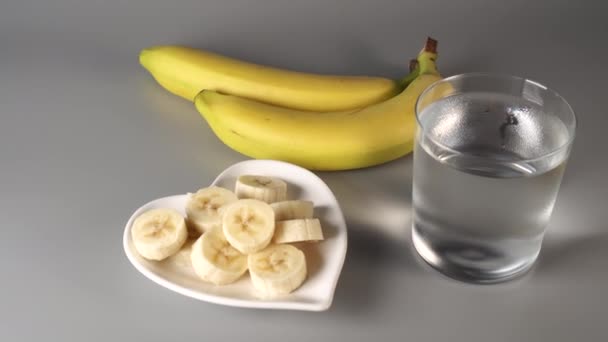 スライスし、バナナ全体。白い皿の上に灰色の背景に表示されます。きれいな水で霧に包まれた。健康的なライフスタイルの概念 - 映像、動画