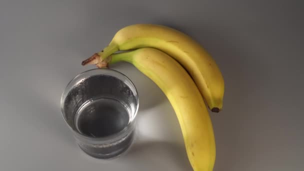 geschnittene und ganze Bananen. auf einem weißen Teller. auf grauem Hintergrund. vernebelt mit sauberem Wasser. Fruchtdiätkonzept - Filmmaterial, Video