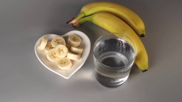geschnittene und ganze Bananen. auf einem weißen Teller. auf grauem Hintergrund. vernebelt mit sauberem Wasser. das Konzept eines gesunden Lebensstils - Filmmaterial, Video