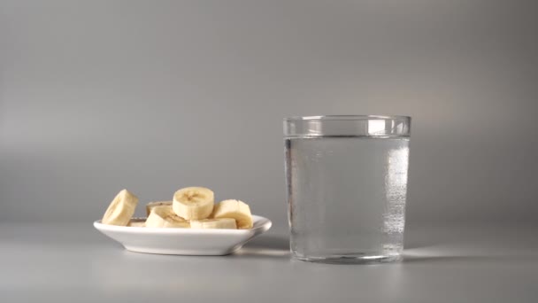 Sliced bananas. On a white plate. On a gray background. Misted up with clear water. The concept of dietary fruit ecological nutrition - Imágenes, Vídeo