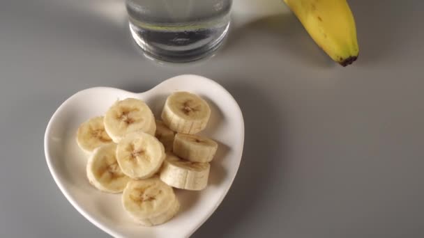 Sliced and whole bananas. On a white plate. On a gray background. Misted with clean water. Fruit diet concept - Materiał filmowy, wideo