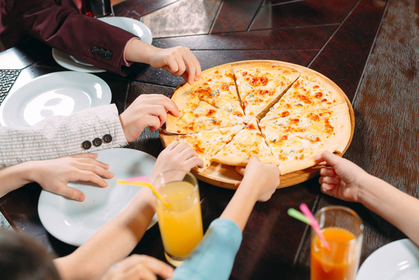 Hands taking pizza slices from wooden table, close up view. - Фото, изображение