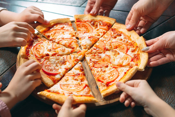Manos tomando rebanadas de pizza de mesa de madera, vista de cerca
. - Foto, Imagen