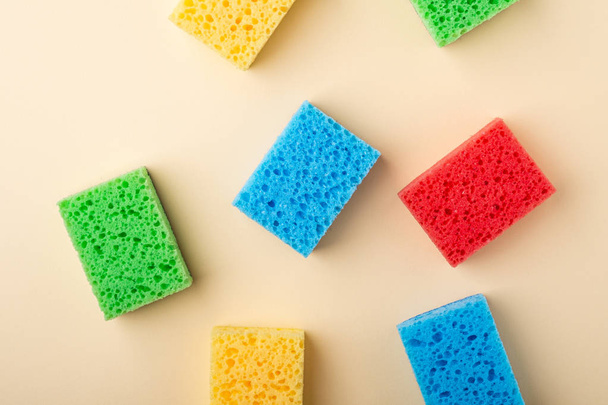 Yellow, green, red, blue sponges on cream colored paper background, copy space, top view, flat lay - Фото, изображение
