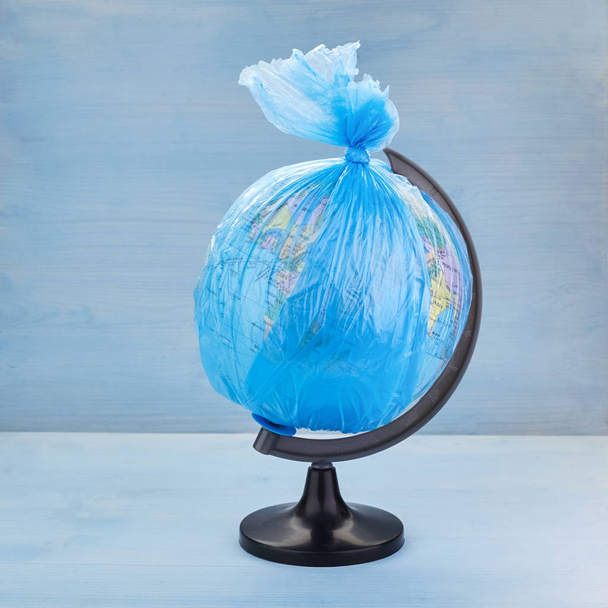 Globe of planet Earth dressed in a garbage plastic bag on blue wooden background - Photo, Image