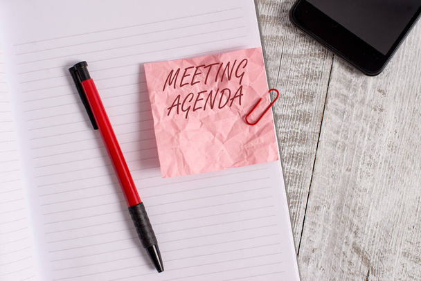 Conceptual hand writing showing Meeting Agenda. Business photo text An agenda sets clear expectations for what needs to a meeting Wrinkle paper notebook and stationary placed on wooden background. - Photo, Image