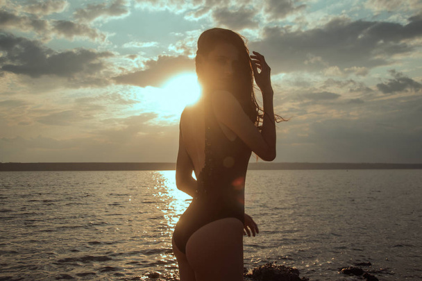 Impressionante bela menina de cabelo escuro despojado em maiô no pôr do sol na praia
 - Foto, Imagem
