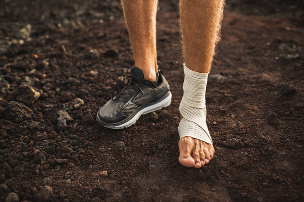 Мужская лодыжка в компрессионной повязке. Травма ноги во время бега по тропе
 - Фото, изображение