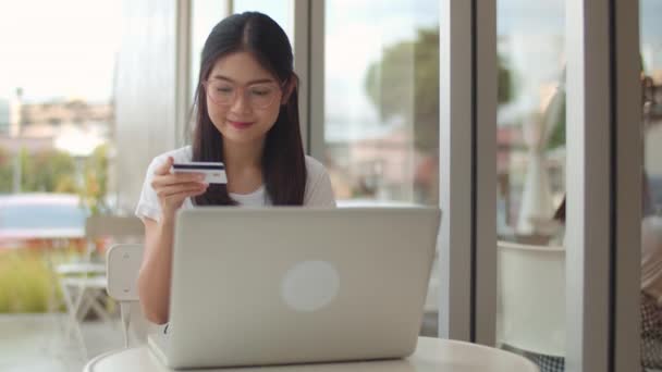 Freelance Asian women online shopping at coffee shop. Young Asia Girl using laptop, credit card buy and purchase e-commerce on internet on table at an outdoor cafe in evening concept. Slow motion - Felvétel, videó