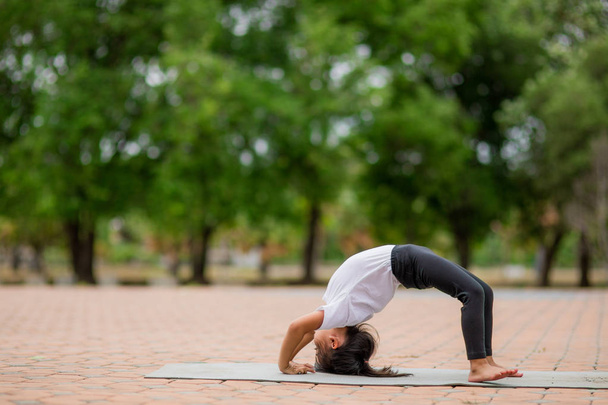 Kis aranyos lány gyakorló jóga pózol egy szőnyegen a parkban, he - Fotó, kép