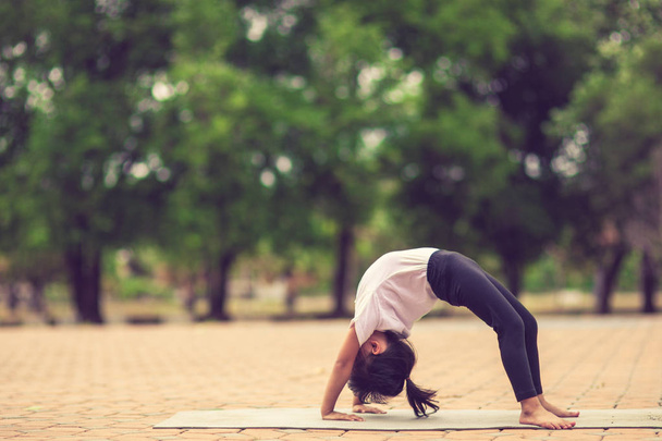 Little cute asian girl practicing yoga pose on a mat in park, He - Photo, Image
