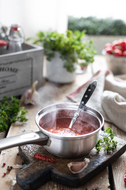 The process of making hot red tomato sauce. Ingredients: tomato, herbs, basil, paprika on a wooden table. Glass jars with ready-made sauce - Zdjęcie, obraz