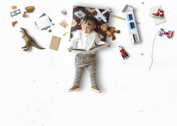 Little cute boy lying and reading a book among his toys - Photo, Image