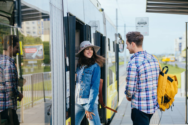Stylish couple of travelers with backpacks entering into tram at outdoor tram stop. - Photo, Image