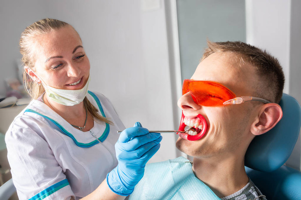 Стоматология. Веселая женщина-дантист и молодой пациент-мужчина. Исследование зубов с помощью зубного зеркала крупным планом
. - Фото, изображение