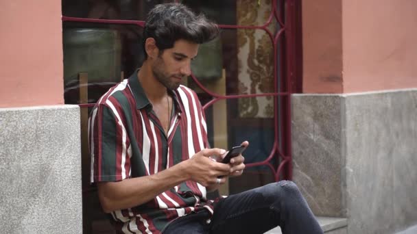 Hombre joven usando el teléfono inteligente sentado en el paso urbano
. - Imágenes, Vídeo