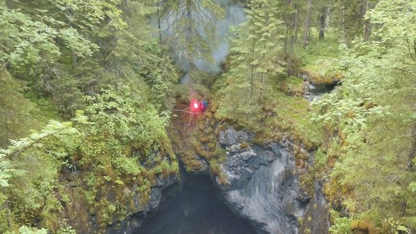 Letecký pohled na člověka stojícího na okraji hluboké rokle s červeným světlým signálem v lese u vysokých starých stromů a keřů. Skladní záběry. SOS signály v lese - Fotografie, Obrázek