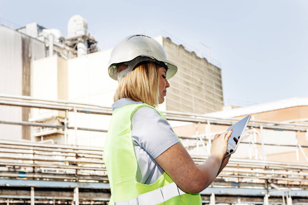 female worker outdoors in a factory holding a tablet. women occupations and industrial jobs concept - Photo, Image