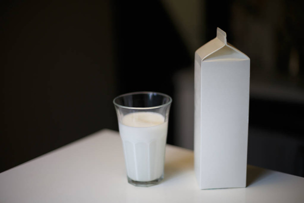 Картонная коробка и стакан молока на столе на кухне - Фото, изображение