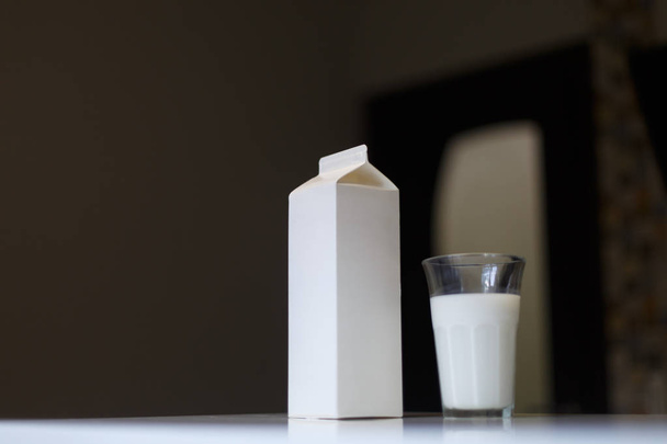 Boîte en carton et verre de lait sur la table dans la cuisine - Photo, image