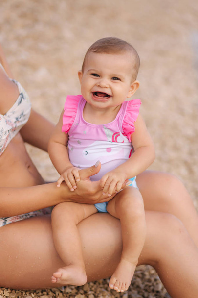 Vauva tyttö istuu äidit polvillaan th rannalla. Nuori kaunis äiti hänen söpö vauva. Lähikuva vauvan hymy
 - Valokuva, kuva