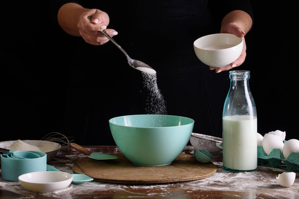 Cook's hands on a dark background pour sugar for dough. The process of making dessert. - 写真・画像