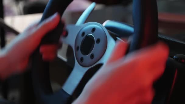 Close-up of the hands of a young gamer behind the steering wheel of a racing simulator and push buttons. Young gamer enjoying car racing video game with a wheel. Computer simulation. - Footage, Video