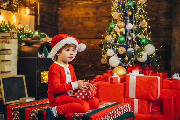 Lovely baby enjoy christmas. Santa boy little child celebrate christmas at home. Family holiday. Boy cute child cheerful mood play near christmas tree. Merry and bright christmas. Opening gift - Photo, image