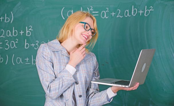Woman teacher wear eyeglasses holds laptop surfing internet. Educator smart clever lady with modern laptop searching information chalkboard background. Learn it easy way. Online schooling concept - Foto, immagini